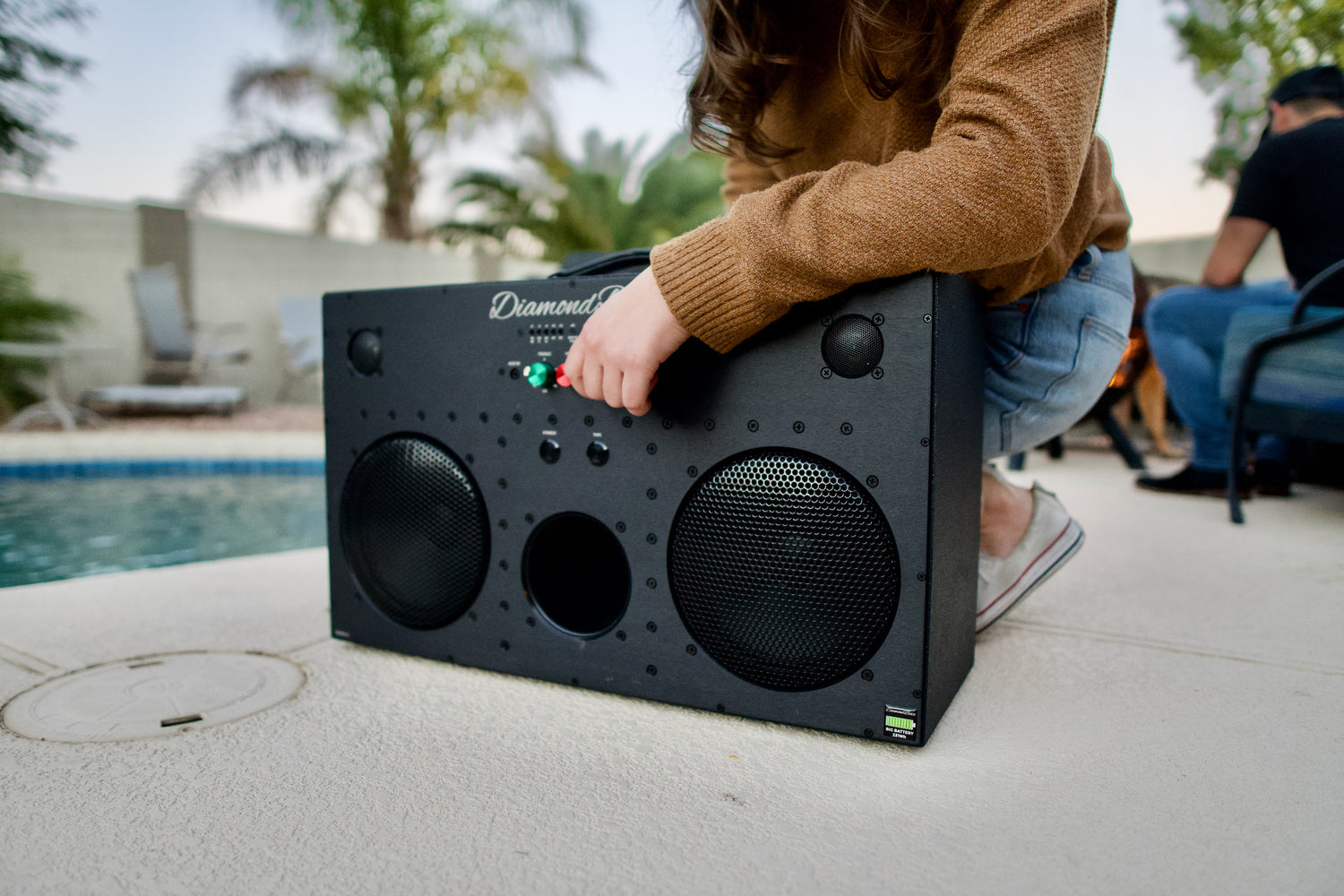 front angled view of L3 speaker black with red and green knobs next to pool with cropped person&
