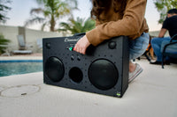 front angled view of L3 speaker black with red and green knobs next to pool with cropped person's arm resting on top