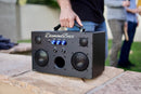 black M3 speaker with blue knobs in outdoor setting with man's hand gripping the handle