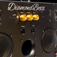 zoomed in view of diamondboxx logo, power, and tws buttons on the front of black M3 speaker with gold knobs